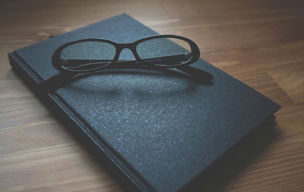 Black notebook with eyeglasses on a wooden surface, capturing a professional and classic vibe.